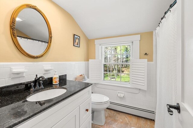 bathroom featuring tile walls, wainscoting, vanity, a baseboard heating unit, and lofted ceiling