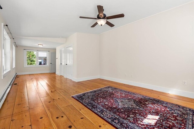 unfurnished room featuring a barn door, light wood finished floors, a ceiling fan, baseboards, and a baseboard heating unit