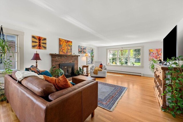 living room with a brick fireplace, baseboard heating, and light wood-style flooring