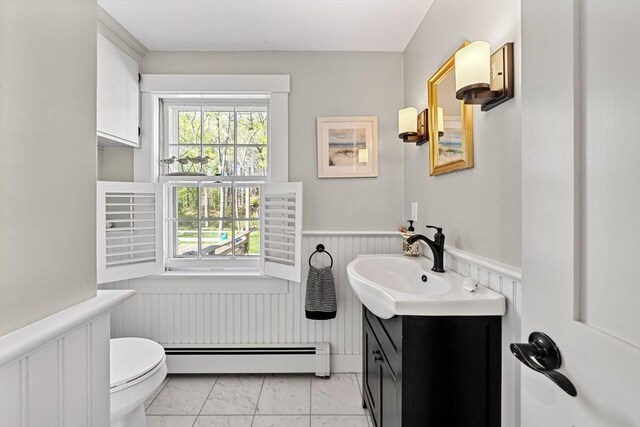 bathroom featuring baseboard heating, wainscoting, vanity, toilet, and marble finish floor