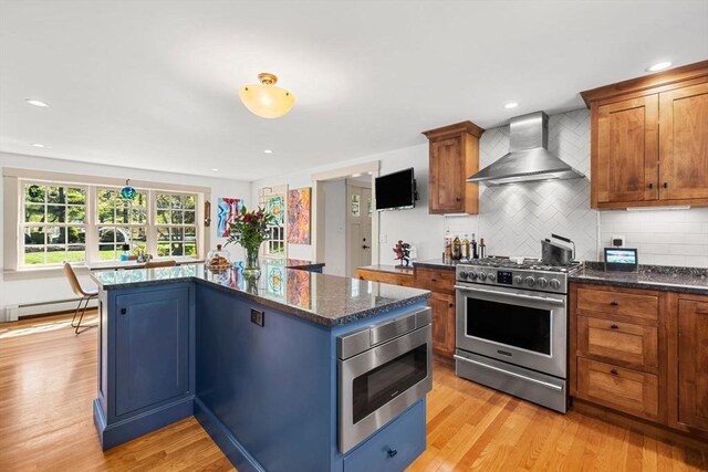 kitchen with wall chimney range hood, tasteful backsplash, baseboard heating, light wood-style floors, and stainless steel appliances