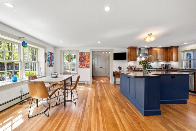 kitchen featuring dark countertops, baseboard heating, stainless steel dishwasher, light wood-style flooring, and wall chimney exhaust hood