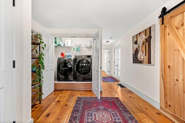 laundry room with laundry area, a barn door, light wood-style flooring, and washer and clothes dryer