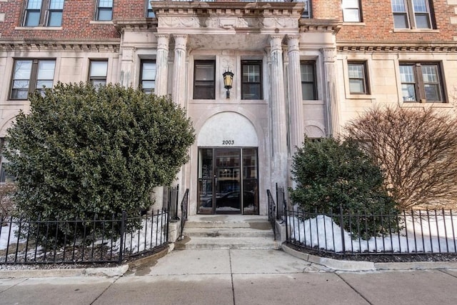 view of exterior entry featuring fence and brick siding