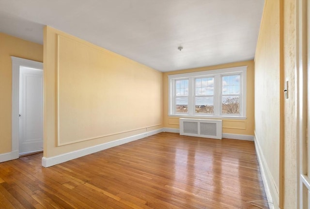 unfurnished room featuring baseboards, radiator heating unit, and hardwood / wood-style flooring