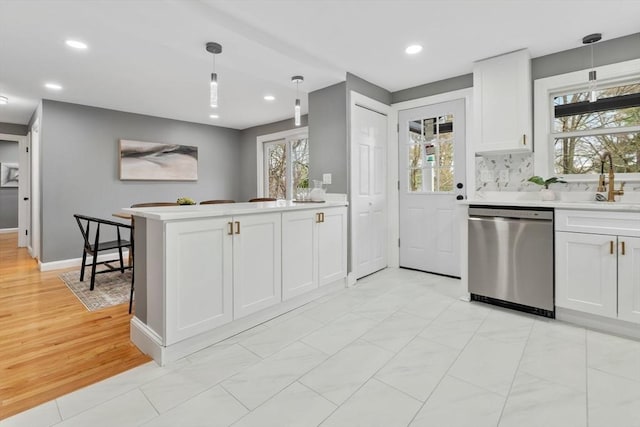 kitchen with stainless steel dishwasher, light countertops, white cabinets, and decorative light fixtures