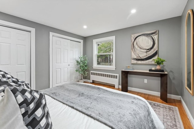 bedroom with radiator, wood finished floors, two closets, baseboards, and recessed lighting