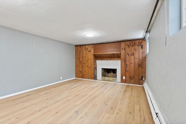 unfurnished living room featuring a fireplace, wood walls, light wood-style flooring, baseboards, and a baseboard heating unit