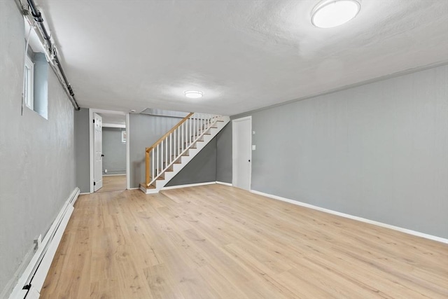 below grade area featuring stairs, baseboards, baseboard heating, and light wood-type flooring