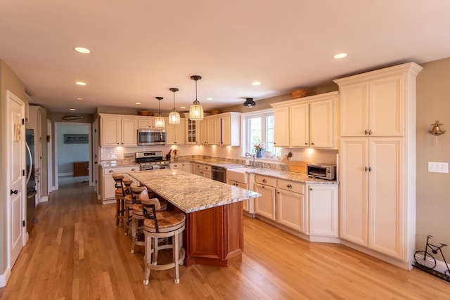 kitchen featuring light wood-type flooring, pendant lighting, light stone counters, a center island, and appliances with stainless steel finishes