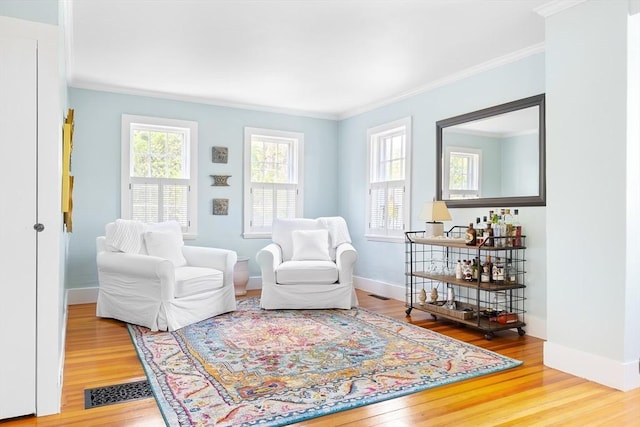 living area featuring visible vents, baseboards, crown molding, and wood finished floors