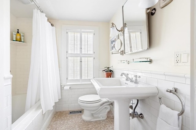 bathroom with tile walls, tile patterned flooring, toilet, and a wealth of natural light