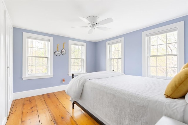bedroom featuring baseboards, a ceiling fan, light wood-style floors, and multiple windows