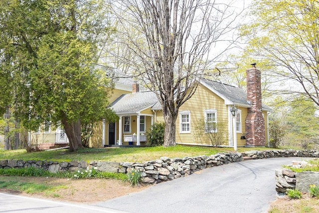 view of front of home featuring covered porch, a chimney, and a front lawn