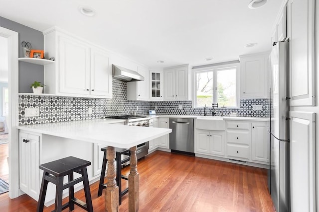 kitchen featuring exhaust hood, open shelves, appliances with stainless steel finishes, a sink, and a peninsula
