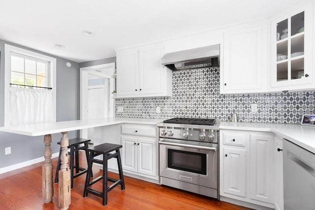kitchen with light countertops, white cabinetry, wall chimney range hood, and stainless steel appliances