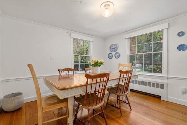 dining area featuring baseboards, ornamental molding, radiator, and light wood-style floors