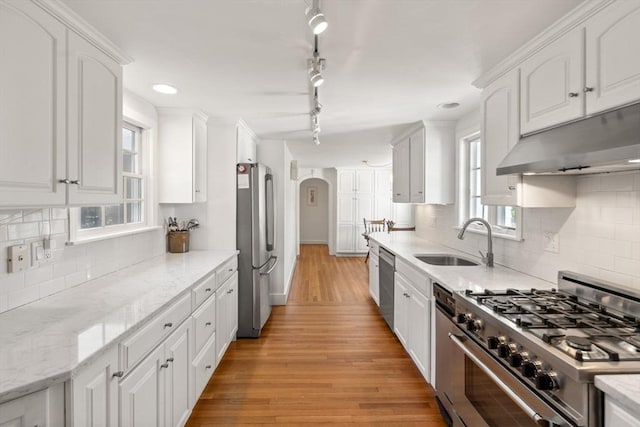 kitchen with arched walkways, a sink, white cabinets, under cabinet range hood, and stainless steel appliances