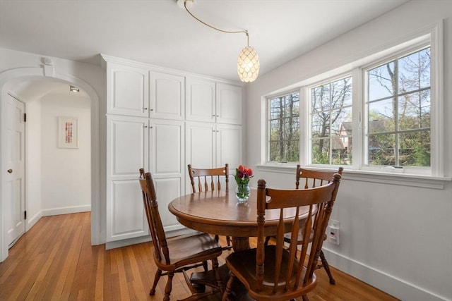 dining space featuring arched walkways, baseboards, and light wood finished floors