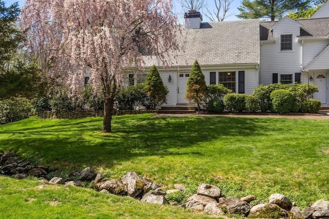 new england style home featuring a chimney and a front lawn
