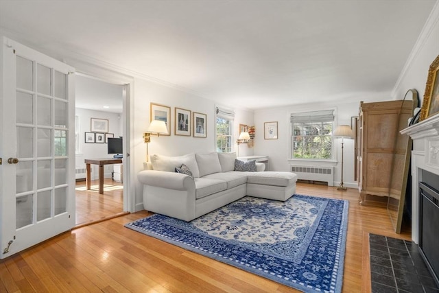 living area featuring a fireplace with flush hearth, radiator, ornamental molding, and wood finished floors