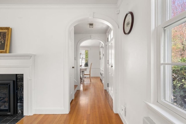hallway featuring crown molding, arched walkways, baseboards, and light wood finished floors