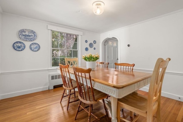 dining space with crown molding, arched walkways, radiator, and light wood finished floors