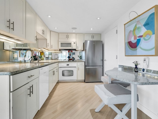 kitchen featuring light hardwood / wood-style flooring, white cabinets, white appliances, and dark stone countertops