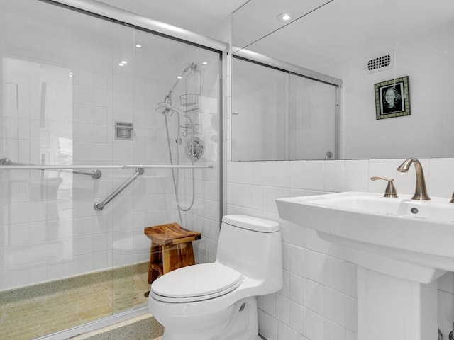 bathroom featuring tile walls, toilet, sink, and a shower with shower door