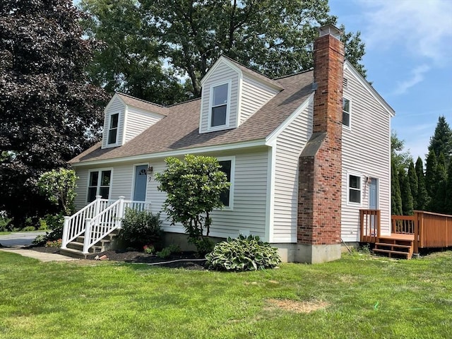 view of front facade featuring a front yard, a chimney, roof with shingles, and a wooden deck