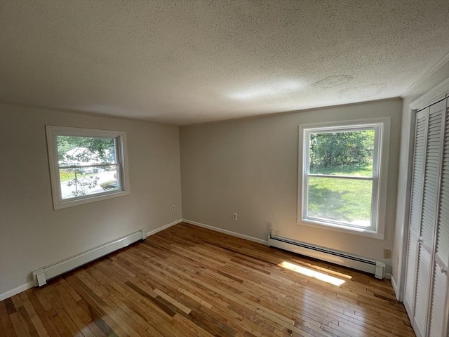 empty room with wood-type flooring, baseboards, baseboard heating, and a textured ceiling