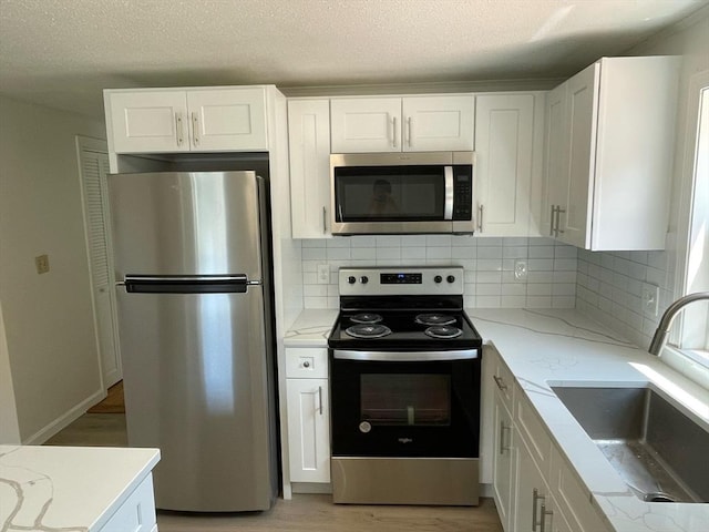 kitchen featuring a sink, light stone counters, light wood-style floors, appliances with stainless steel finishes, and white cabinets