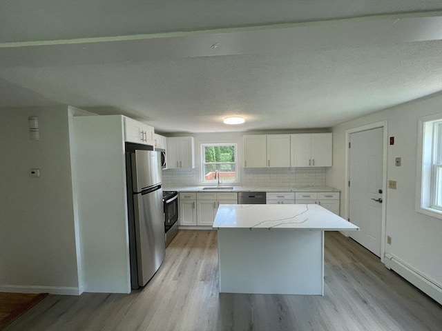 kitchen with tasteful backsplash, baseboard heating, light wood-style flooring, stainless steel appliances, and a sink