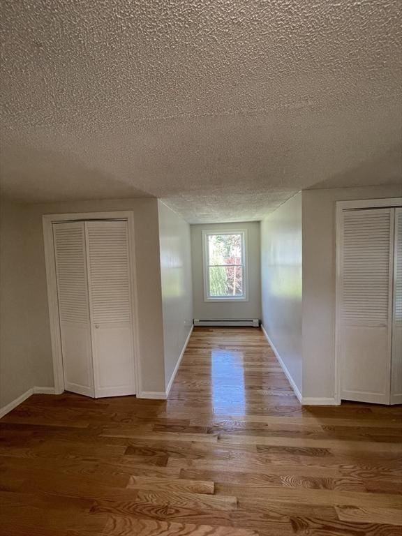 spare room featuring baseboards, baseboard heating, wood finished floors, and a textured ceiling