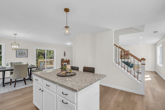 kitchen with white cabinetry, light stone counters, light hardwood / wood-style flooring, decorative light fixtures, and a kitchen island