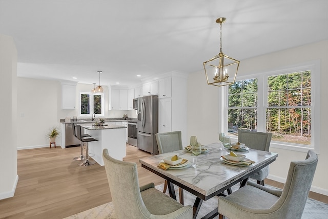 dining area with light wood-type flooring, plenty of natural light, a notable chandelier, and sink