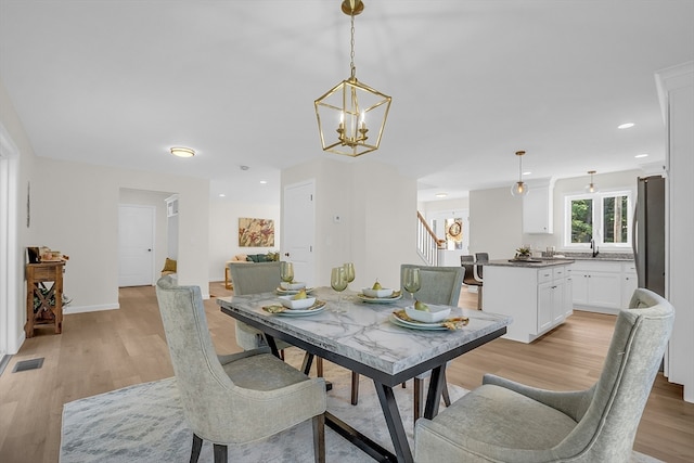 dining space with light wood-type flooring, sink, and an inviting chandelier