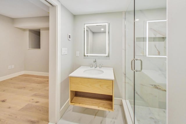 bathroom featuring a marble finish shower, wood finished floors, vanity, and baseboards