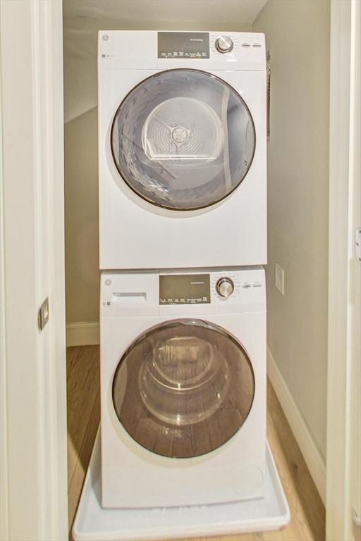 clothes washing area with stacked washer / drying machine, baseboards, and wood finished floors