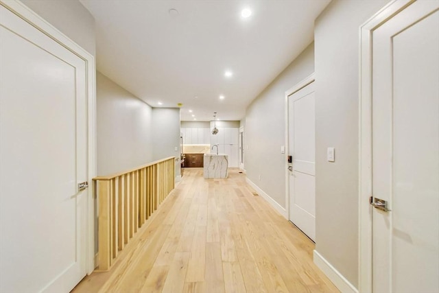 hallway with light wood-style flooring, recessed lighting, a sink, and baseboards