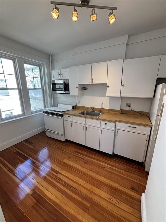 kitchen with a sink, white appliances, white cabinets, baseboards, and dark wood-style flooring