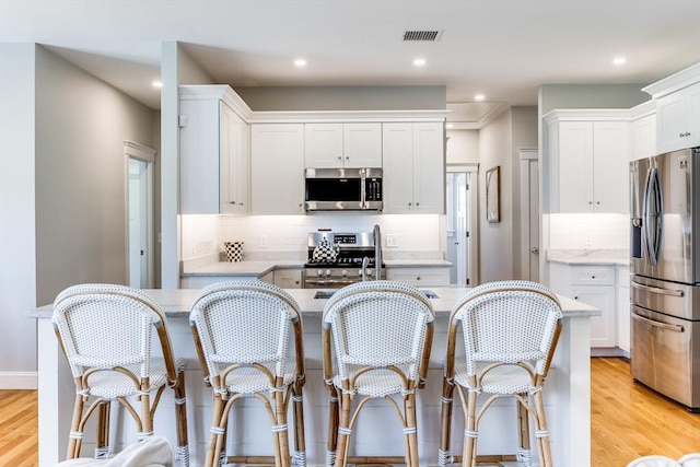 kitchen with stainless steel appliances, light wood-style flooring, backsplash, white cabinets, and recessed lighting
