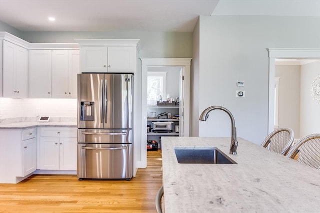 kitchen with stainless steel refrigerator with ice dispenser, a sink, white cabinetry, light stone countertops, and light wood-style floors