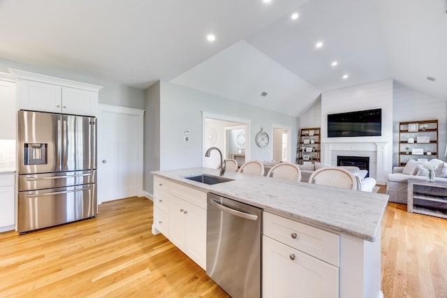 kitchen with stainless steel appliances, a sink, vaulted ceiling, light wood-style flooring, and white cabinetry
