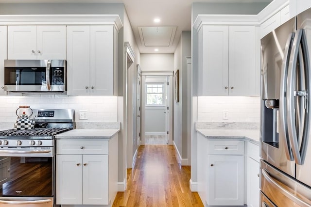 kitchen featuring stainless steel appliances, white cabinetry, baseboards, and light wood finished floors