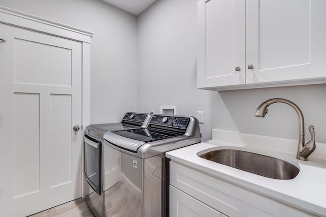 clothes washing area with washing machine and clothes dryer, cabinet space, and light wood-style floors