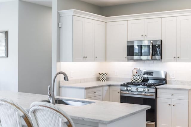 kitchen featuring appliances with stainless steel finishes, a sink, decorative backsplash, light stone counters, and white cabinets