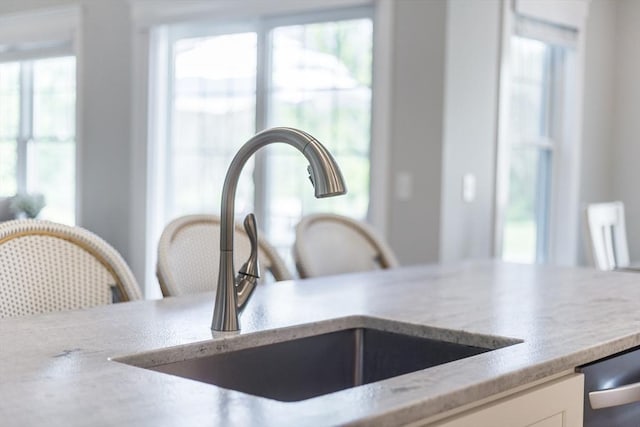 kitchen view of a sink, white cabinetry, and light stone counters
