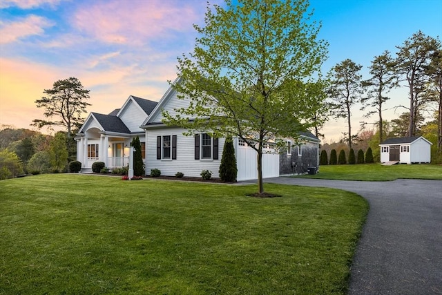 view of front of home featuring asphalt driveway, a front yard, an attached garage, a storage shed, and an outdoor structure