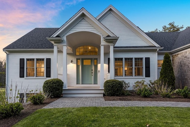 view of front of property featuring roof with shingles, a porch, and a front yard